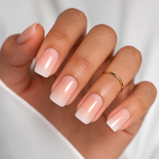 Hand met korte, vierkante kunstnagels in french manicure ombre stijl. De nagels hebben een roze basis die vervaagt naar een witte punt.