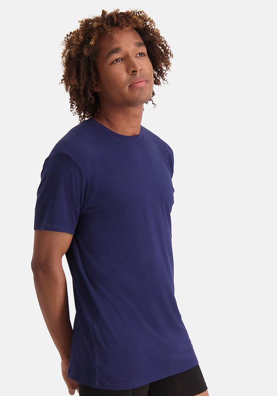 Man draagt een marineblauwe T-shirt met ronde hals, handen achter zijn rug.