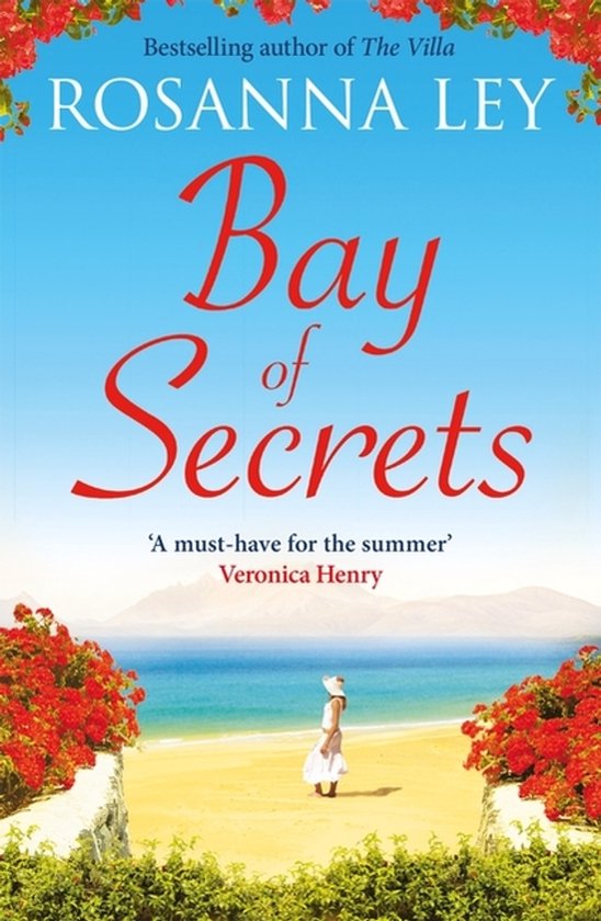 Couverture du livre 'Bay of Secrets' par Rosanna Ley. Une femme en blanc se tient sur une plage ensoleillée avec des fleurs rouges au premier plan et la mer à l'arrière-plan.