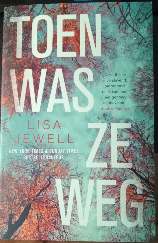 Couverture du livre avec le titre 'TOEN WAS ZE WEG' en grandes lettres blanches sur fond d'arbres et de feuilles aux couleurs d'automne et d'un ciel turquoise. En dessous, le nom LISA JEWELL et le texte 'NEW YORK TIMES & SUNDAY TIMES BESTSELLAATEUR'.