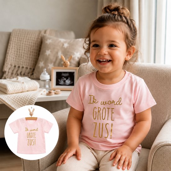 Lachend jong meisje met bruin haar in een knot, zittend in een stoel, draagt een lichtroze t-shirt met gouden tekst 'Ik word GROTE ZUS!'.