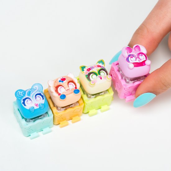 Vier Clickeez figuurtjes met grote ogen en gezichtsuitdrukkingen: blauw met ijzel, beige met bloemen, geel met bloemen en roze met strik.