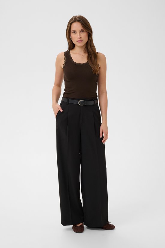 Model in een bruine, nauwsluitende tanktop met kanten rand, gedragen met zwarte wijde broek.