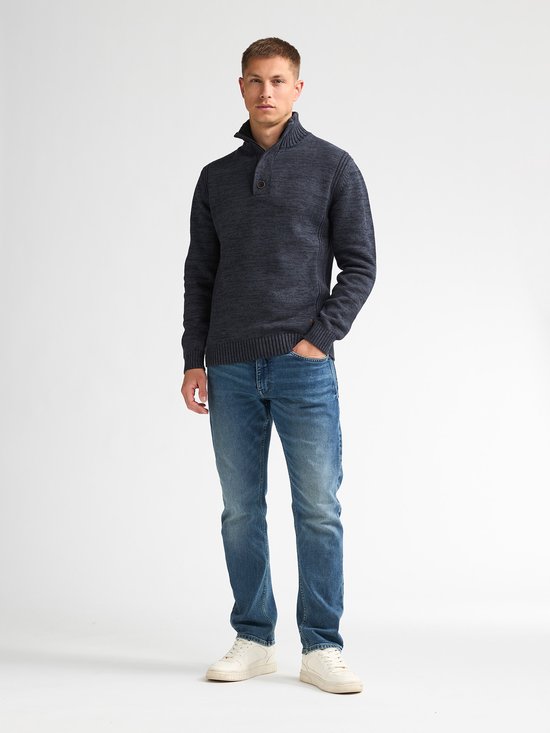 Model draagt een donkerblauwe gebreide trui met opstaande kraag en knoopjes, gecombineerd met jeans.