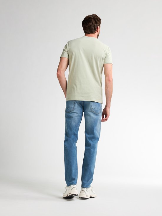 Man van achteren gezien in een lichtgroen T-shirt en lichtblauwe jeans.