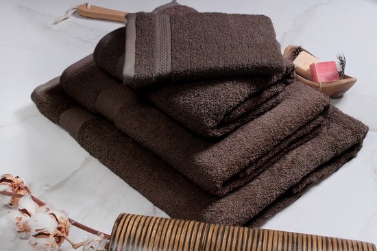 Stapel chocoladebruine handdoeken met textuur, op een marmeren ondergrond met katoenbloesem en zeep.