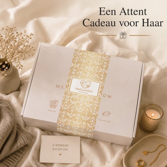 Wit HerComfort kussen in geschenkdoos met gouden patronen, op een bed met sfeervolle verlichting.