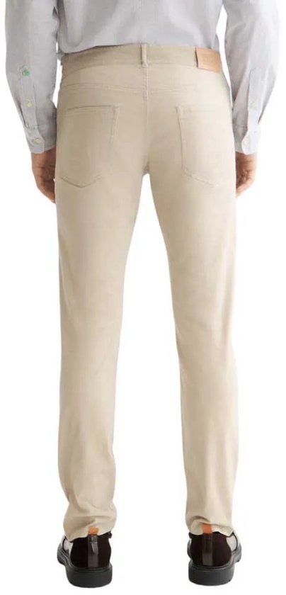 Man in beige corduroy broek, achterkant, met licht gestreepte blouse en bruine schoenen.