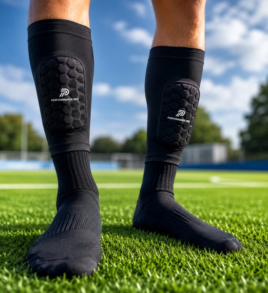Zwarte scheenbeschermer sleeves met ingebouwde pads en Performance Pro logo, gedragen door een persoon op een sportveld.