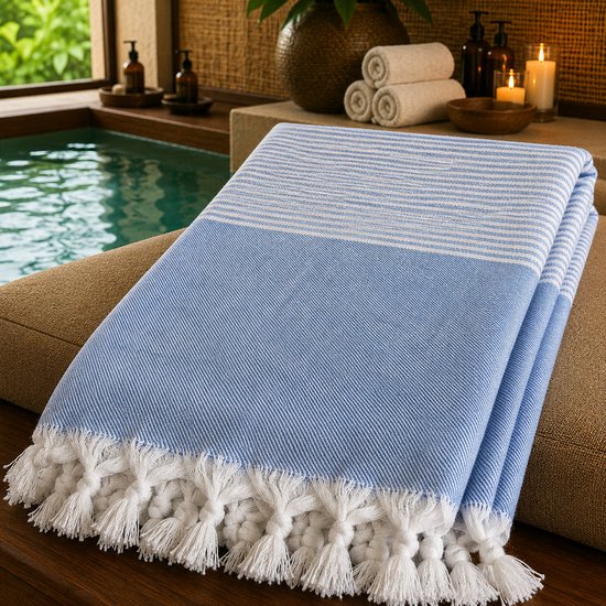 Blauw en wit gestreepte peshtemal met dikke witte franjes, gevouwen op een bruin kussen.
