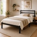 Zwart metalen bedframe met lattenbodem, opgemaakt met wit beddengoed en een beige plaid.