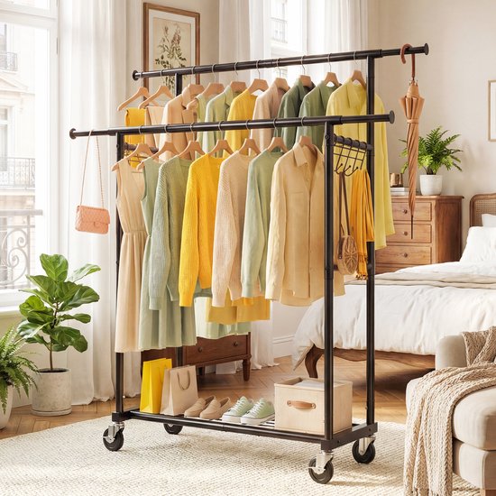 Kledingrek met kleding, schoenen en accessoires in een slaapkamer. Zwart rek, gele en groene kleding.