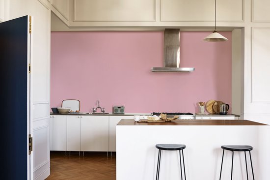 Keuken met witte kasten, fornuis en roze accentmuur.