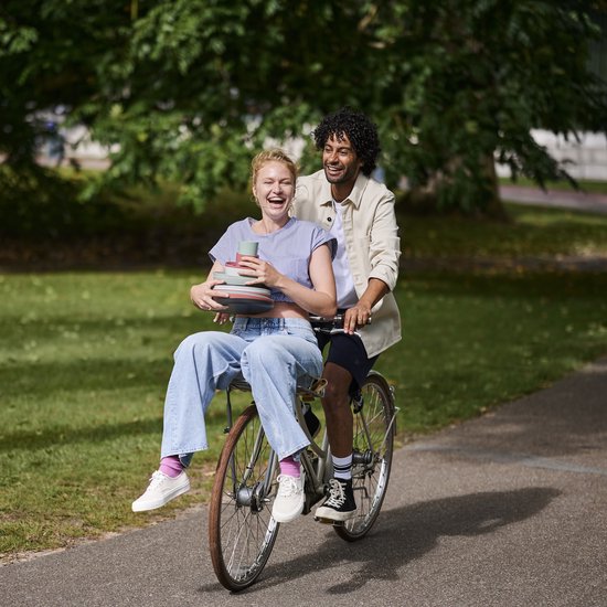 Vrouw op fiets met gestapelde zachtgroene mokken in haar schoot.