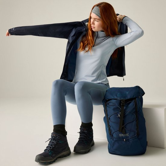 Model dat een donkerblauwe regenjas aantrekt, met een lichtblauwe top, legging en wandelschoenen.