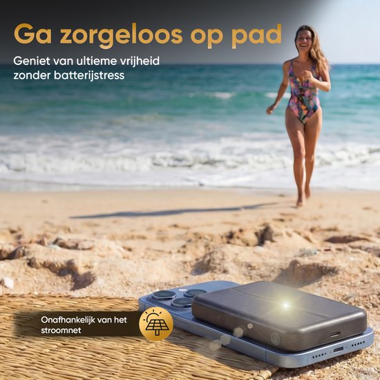 Zonnepaneel powerbank ligt naast een smartphone op een handdoek op het strand. Een vrouw rent in de zee.