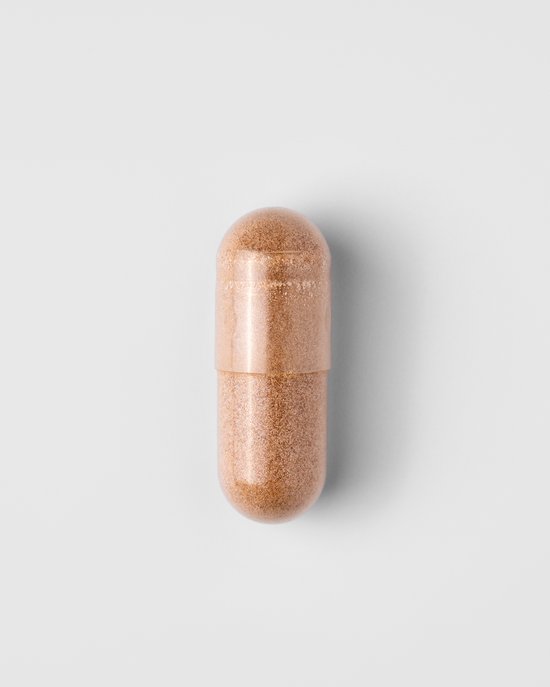 Een enkele lichtbruine capsule met een glanzend oppervlak, op een witte achtergrond.