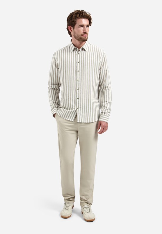 Model draagt een beige overhemd met verticale, brede witte en taupe strepen. Hij draagt er een beige pantalon bij.
