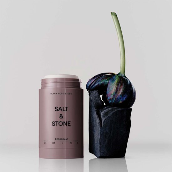 Lichtroze Salt & Stone deodorantstick naast een donkere, puntige steen met een paarse, gedraaide bloem.