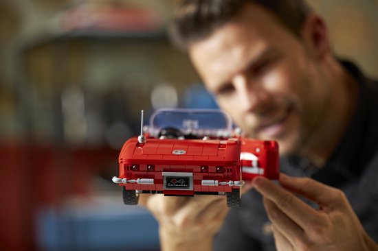 Een man houdt een rode LEGO Chevrolet Corvette cabriolet uit de jaren 60 vast. De achterkant met kentekenplaat is zichtbaar.
