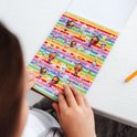 Meisje bekijkt een stickerboek met regenboogkleuren en afbeeldingen van Gabby en katten.