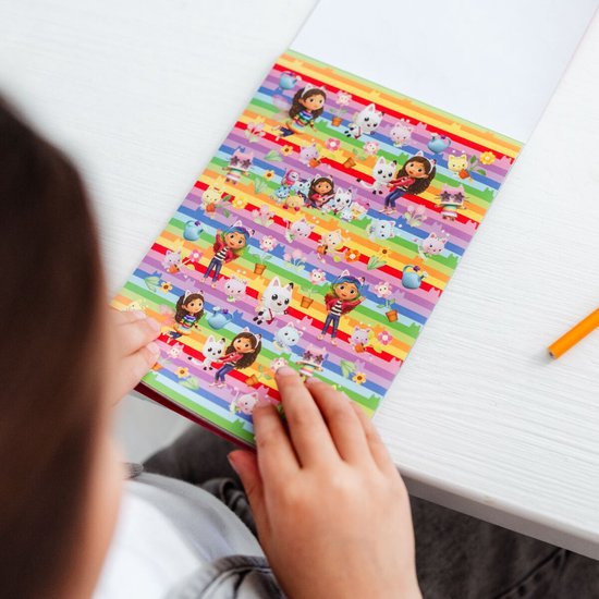 Meisje bekijkt een stickerboek met regenboogkleuren en afbeeldingen van Gabby en katten.
