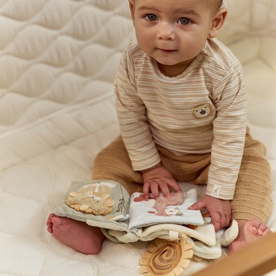 Baby kijkt naar het stoffen boekje. Het boekje is opengevouwen en toont een leeuw en flamingo.