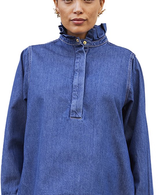 Model draagt een blauwe denim blouse met lange mouwen, opstaande kraag met ruches, knoopsluiting en gouden knopen.