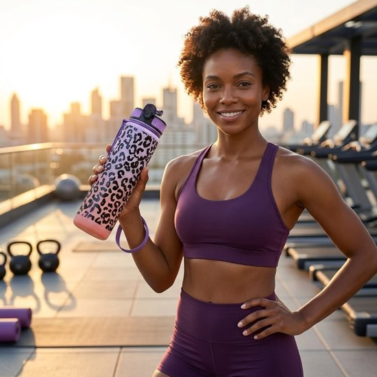 Sportieve vrouw houdt een paars-roze waterfles met luipaardprint vast op een dakterras met fitnessapparatuur.