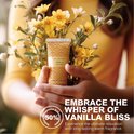 Een hand houdt een kleine tube handcrème met 'Spa Luxetique Vanilla Hand Cream' vast, omringd door gele bloemen.