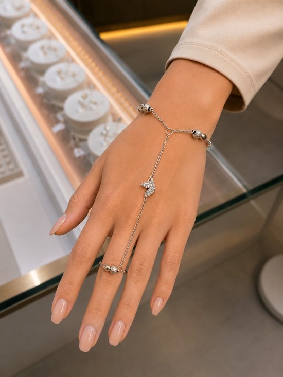 Vingerarmband van zilver met vlinderbedel en bolletjes, gedragen op een hand.