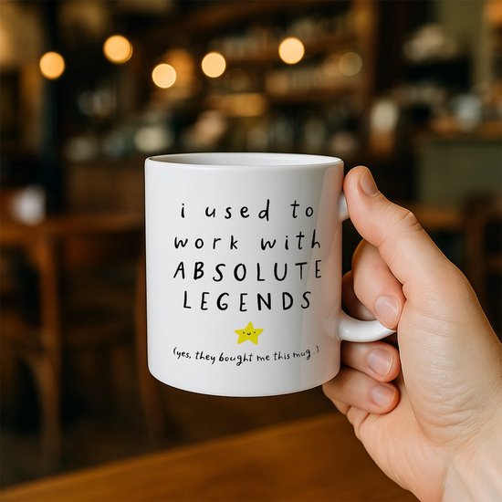 Hand houdt witte mok vast met tekst 'i used to work with ABSOLUTE LEGENDS' en een gele ster.