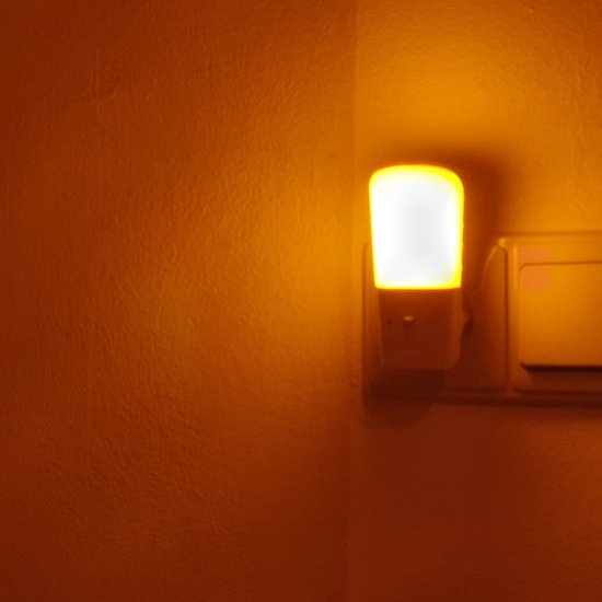 Wit nachtlampje met oranje gloed in een hoekstopcontact, naast een lichtschakelaar.