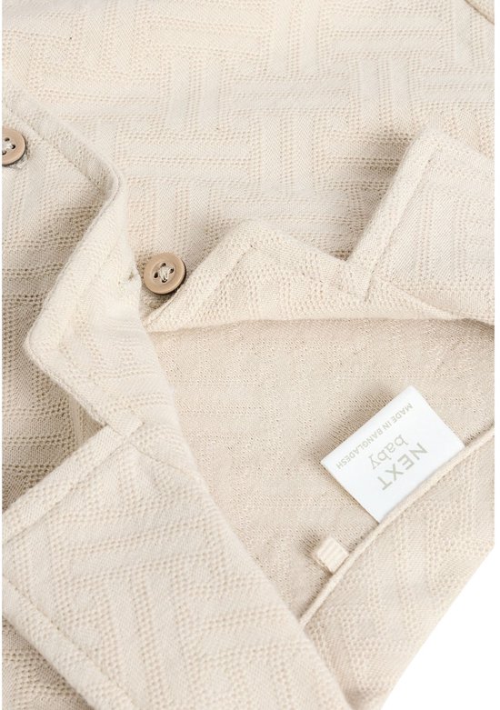 Close-up van beige babyromper met visgraatpatroon, knopen en label.