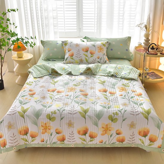 Een bed opgemaakt met groen beddengoed en een lichtgroen dekbed met een bloemenprint van gele en oranje bloemen en groene bladeren. Kussens met hetzelfde patroon.