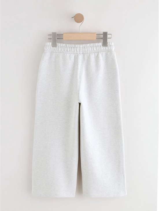 Lichtgrijze wijde joggingbroek met elastische tailleband en trekkoord, hangend aan een kledinghanger.