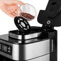 Hand voegt koffiebonen toe aan het filter van het zilverkleurige koffiezetapparaat.