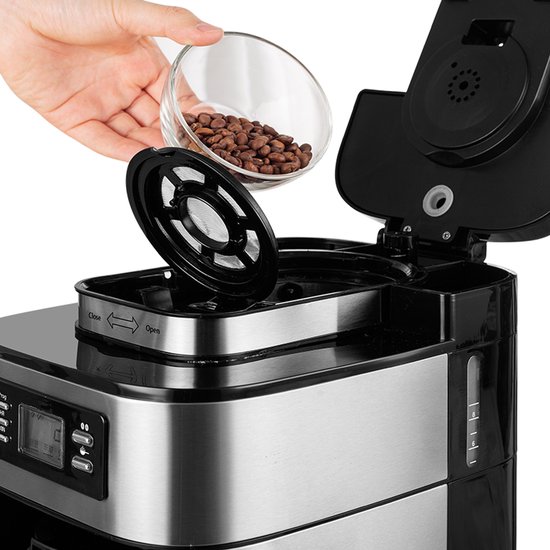Hand voegt koffiebonen toe aan het filter van het zilverkleurige koffiezetapparaat.