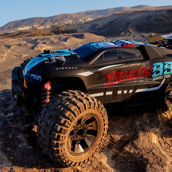 Zwarte RC monster truck met blauwe en rode "Troublemaker Double Eight" graphics. Grote offroad banden en rode schokdempers.