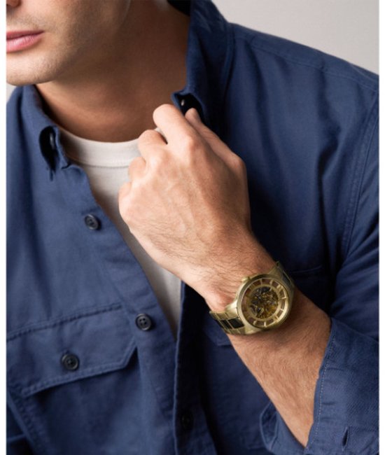 Man met een goudkleurig Fossil skeleton horloge met zichtbare mechaniek om de pols.