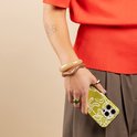 Een vrouw houdt een telefoon vast met een lichtgroen hoesje met wit bloemenpatroon.