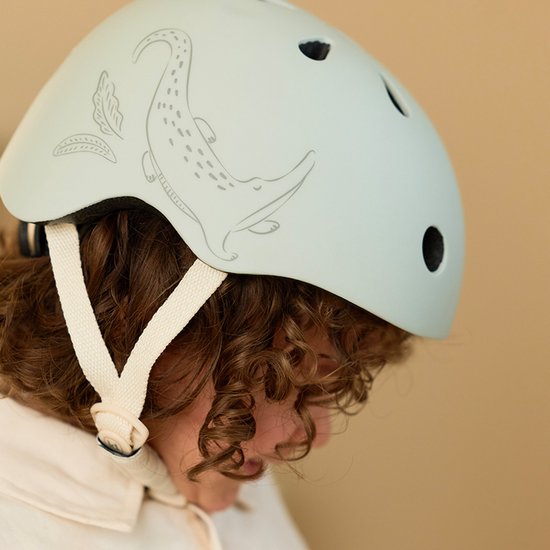 Lichtgroene kinderhelm met krokodillenprint, gedragen door een kind met krullend haar.