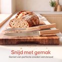 Twee Broba broodmessen met gekartelde bladen en houten handvatten liggen op een houten snijplank naast een vers brood. "Snijd met gemak"