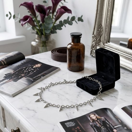 Zilverkleurige schakelketting choker met zeven puntige spikes, op een marmeren tafel naast een open tijdschrift met modellen.