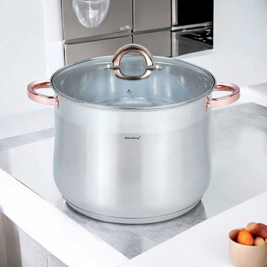 Zilverkleurige soeppan met glazen deksel en koperkleurige handvatten, staand op een aanrecht.
