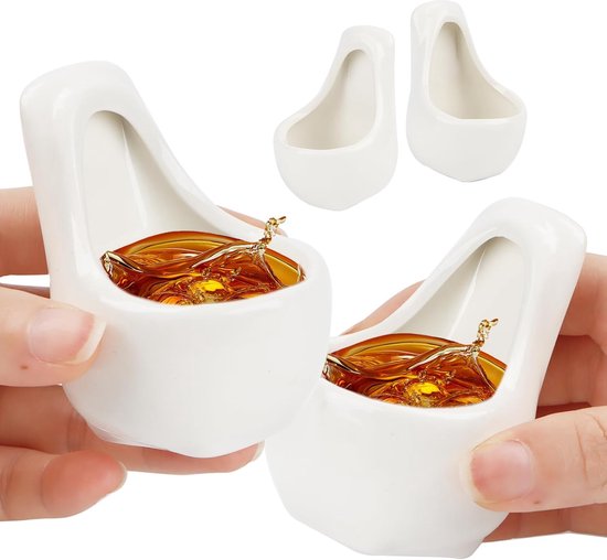 Twee witte keramische urinoir-vormige borrelglaasjes gevuld met amberkleurige drank, vastgehouden door handen.