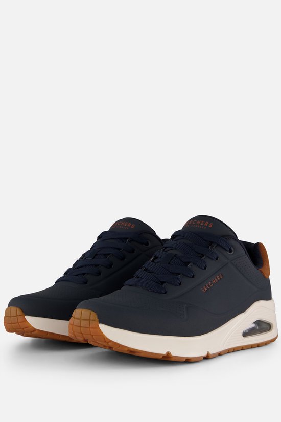 Paar donkerblauwe Skechers sneakers met bruine suède hielkappen, crèmekleurige zolen en oranje logo's.