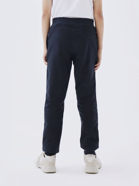 Achterkant van een jongen in donkerblauwe joggingbroek en witte sneakers.