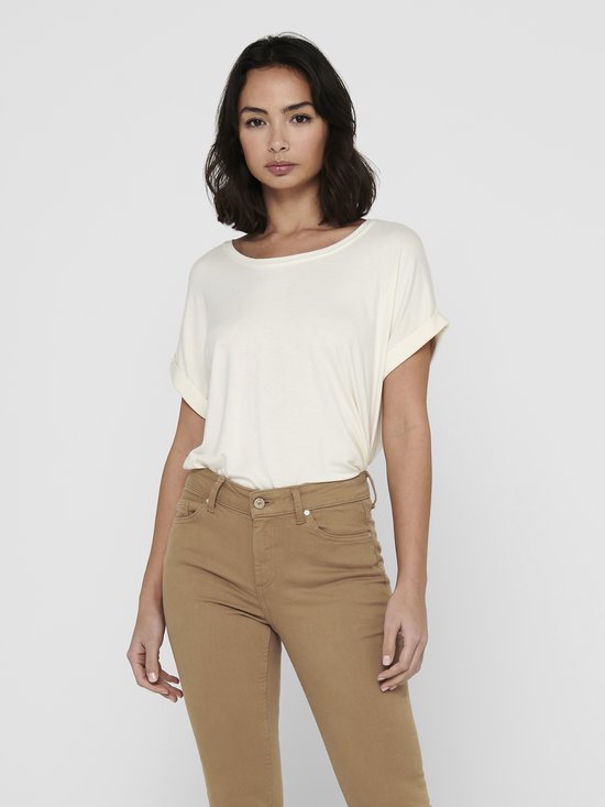 Model in een crèmekleurig T-shirt met opgerolde mouwen en een ronde hals. Draagt een beige skinny broek.