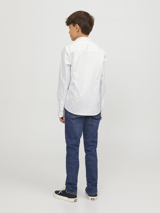 Garçon en chemise blanche à manches longues et jean, debout.